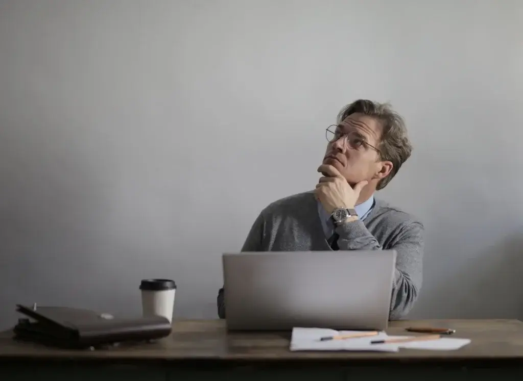Man at a desk with a laptop, looking up in thought about abusive conduct in California