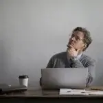 Man at a desk with a laptop, looking up in thought about abusive conduct in California