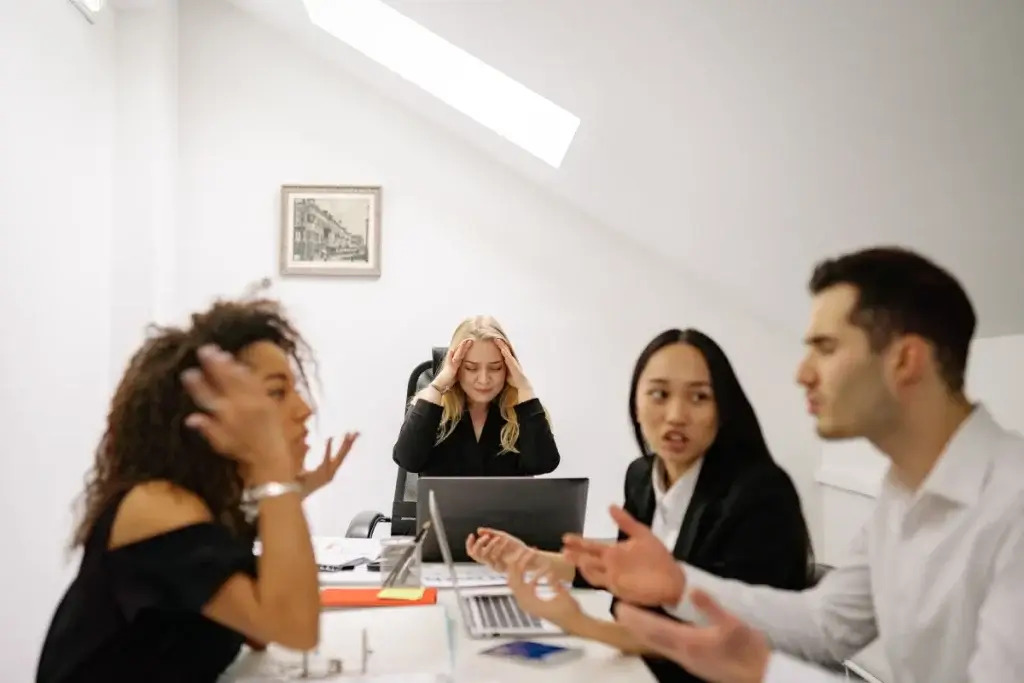 Coworkers arguing at an office table while a stressed colleague holds her head, possible abusive conduct under California law