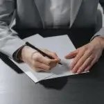 Person in a gray blazer signing a document at a desk, illustrating a resignation under constructive discharge in California