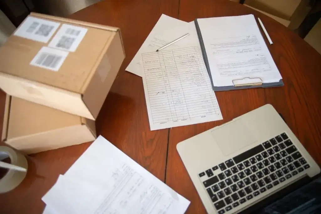 Workers comp and disability claim paperwork on a table beside shipping boxes and a laptop