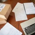 Workers comp and disability claim paperwork on a table beside shipping boxes and a laptop