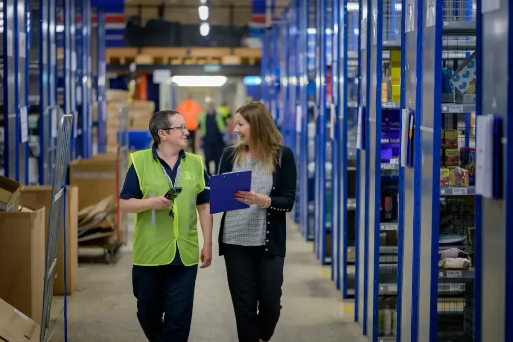 Warehouse worker in a safety vest talking with a coworker, illustrating workers' comp death benefits in California.