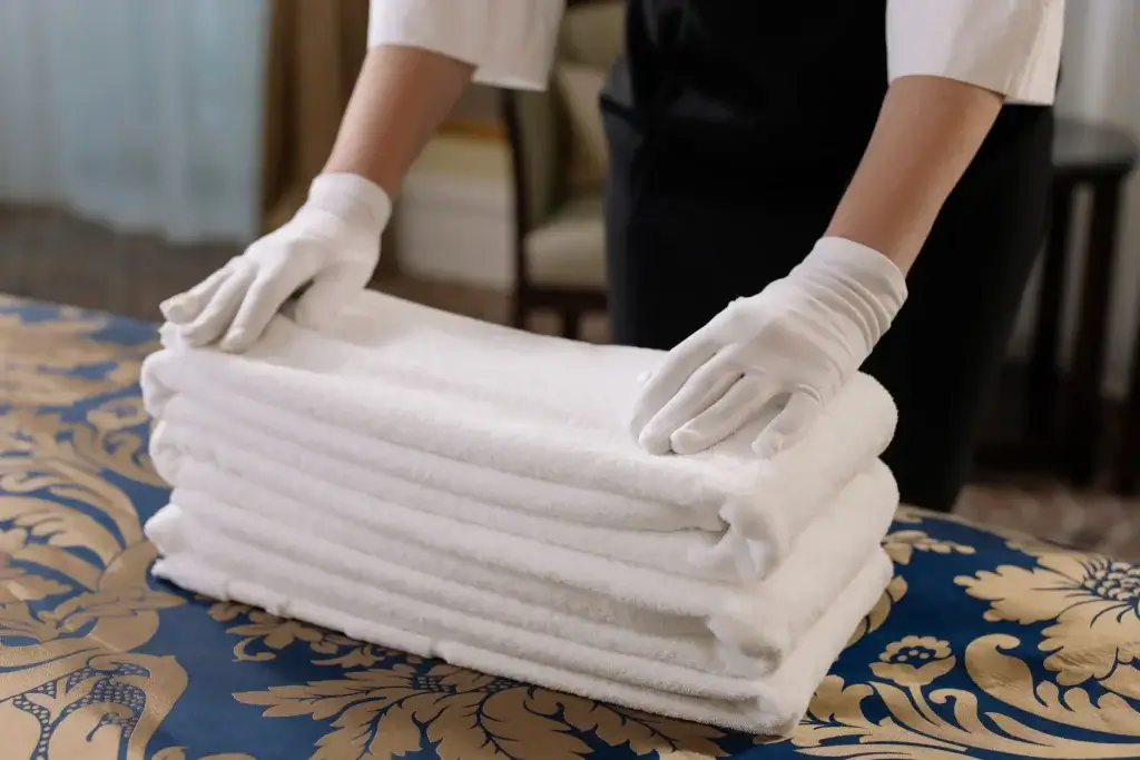 Hotel worker in white gloves stacking fresh towels, a job covered by the LA hotel worker minimum wage