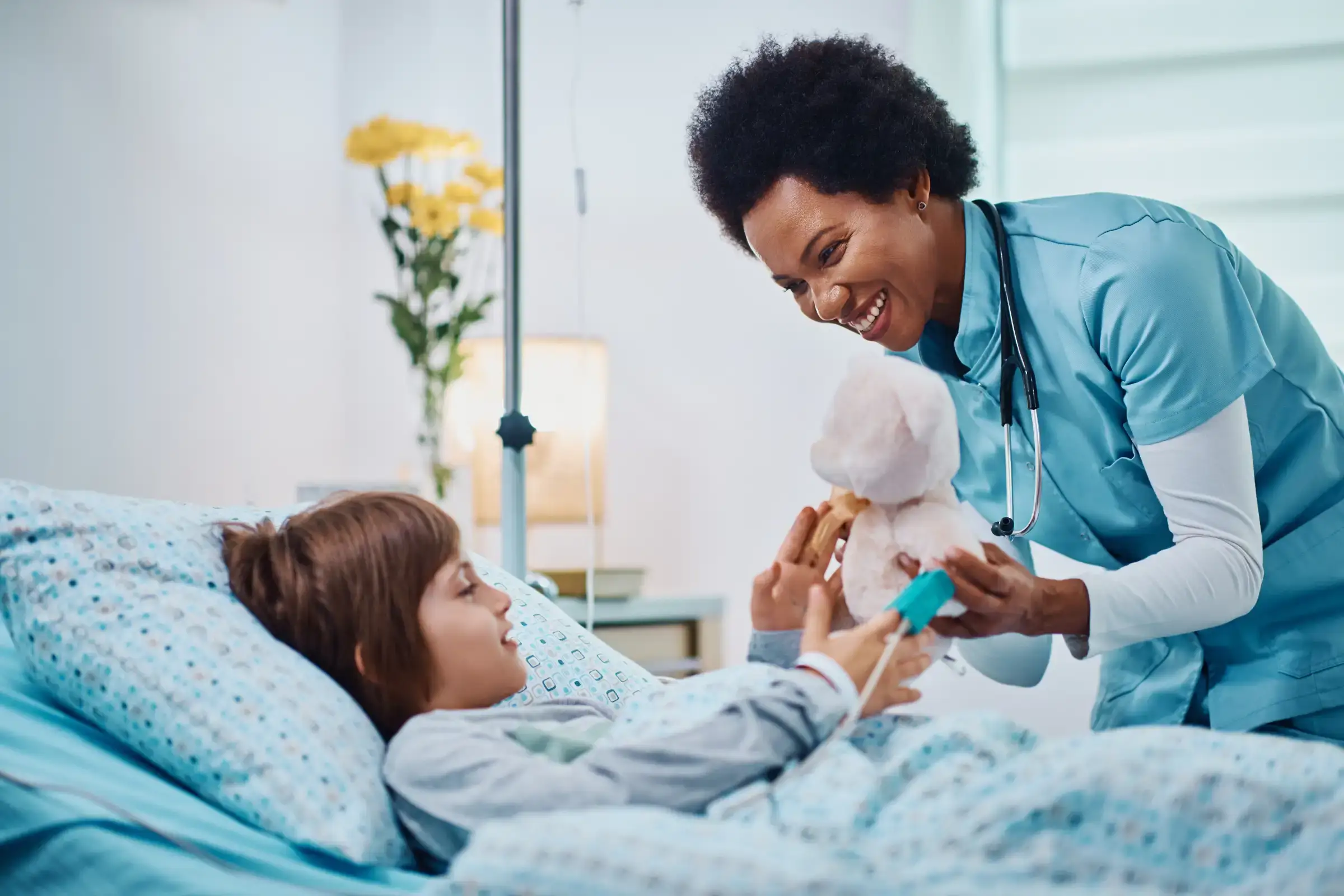 Nurse giving a teddy bear to a child patient in a hospital bed