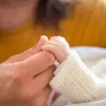 Parent holding a newborn’s hand during paternity leave in California