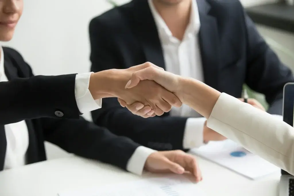 Two people shaking hands across a table after agreeing to a wrongful termination settlement